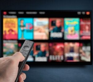 A hand points a smart TV remote at a smart TV screen displaying several blurred-out content titles for viewers to choose from.